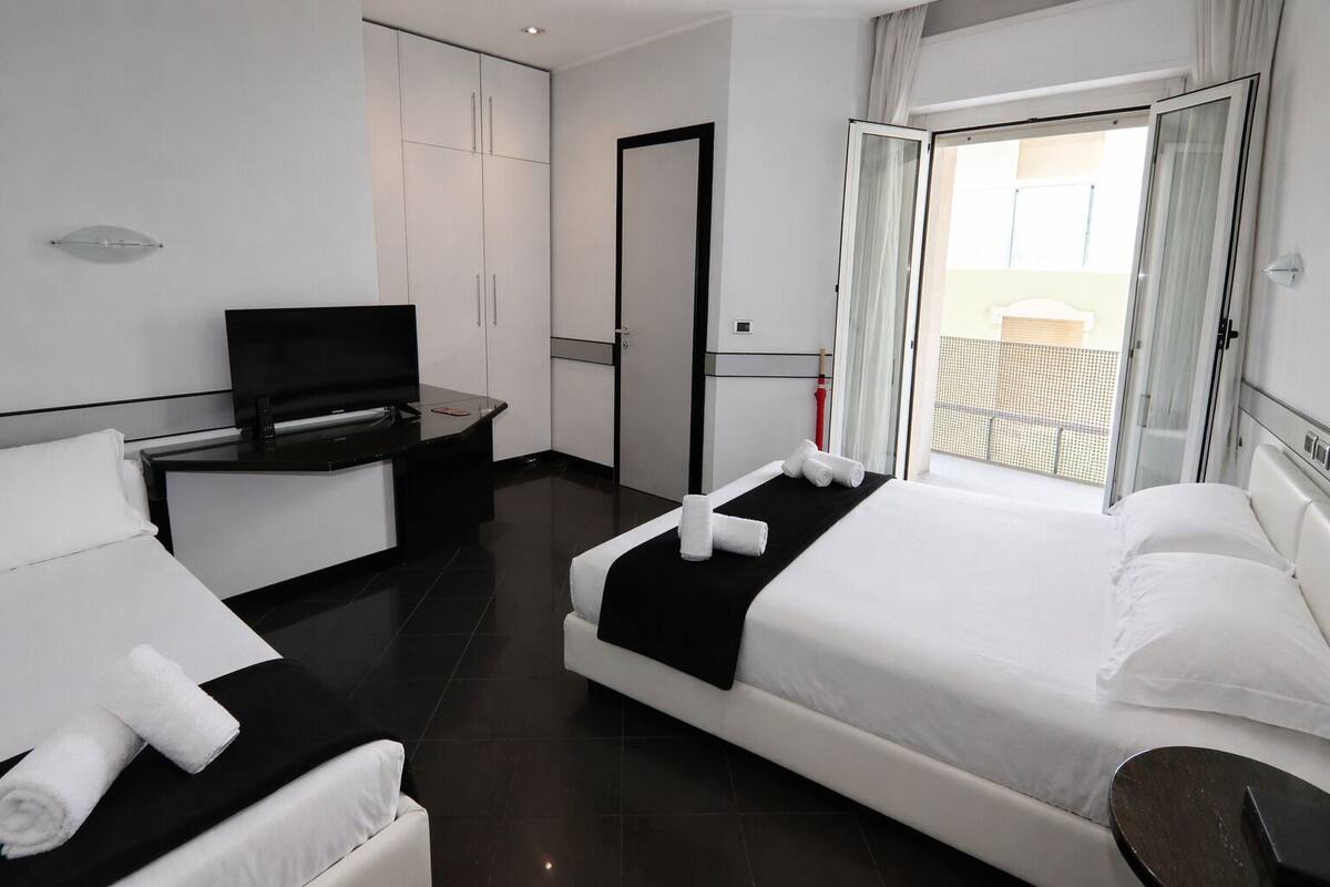 A hotel room with two beds, a TV, a desk, and a balcony with a view.