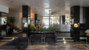 A modern lobby with dark sofas, a glass coffee table, and a bar area with bottles. - Hotel Derby (Rimini)