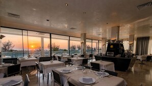 A restaurant with tables set for dining, a buffet area, and a view of the sunset. - Hotel Derby (Rimini)