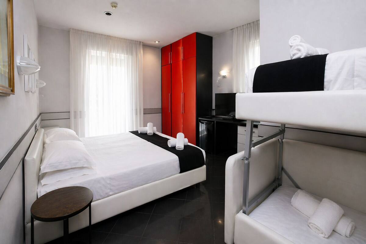 A hotel room with a bed, a desk, a chair, a TV, and a red wardrobe.