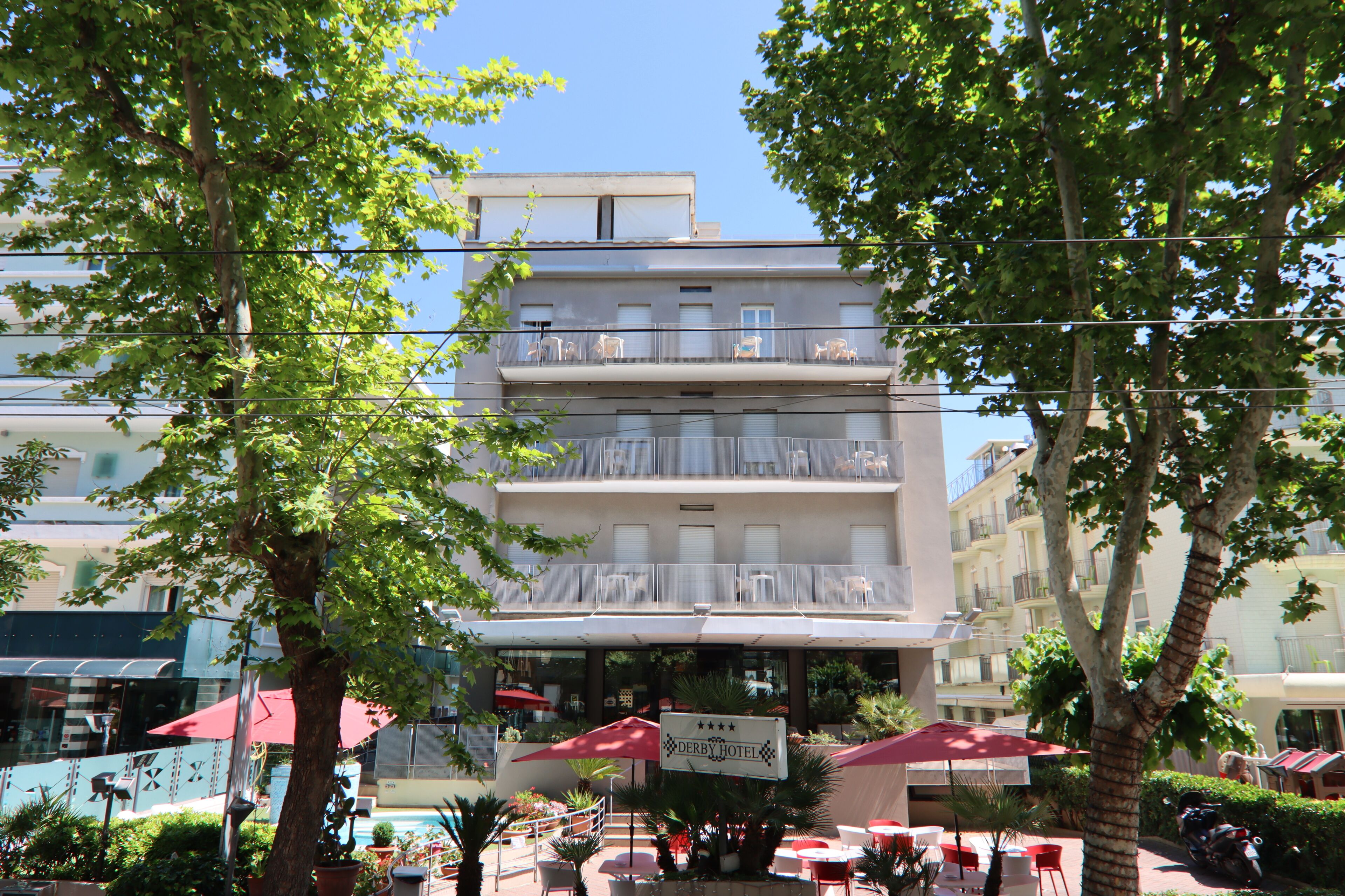 A hotel with outdoor seating, a sign indicating it's a hotel, and balconies with furniture.