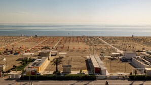 A beach with rows of umbrellas and beach chairs, a few buildings, and a clear view of the sea. - Hotel Derby (Rimini)