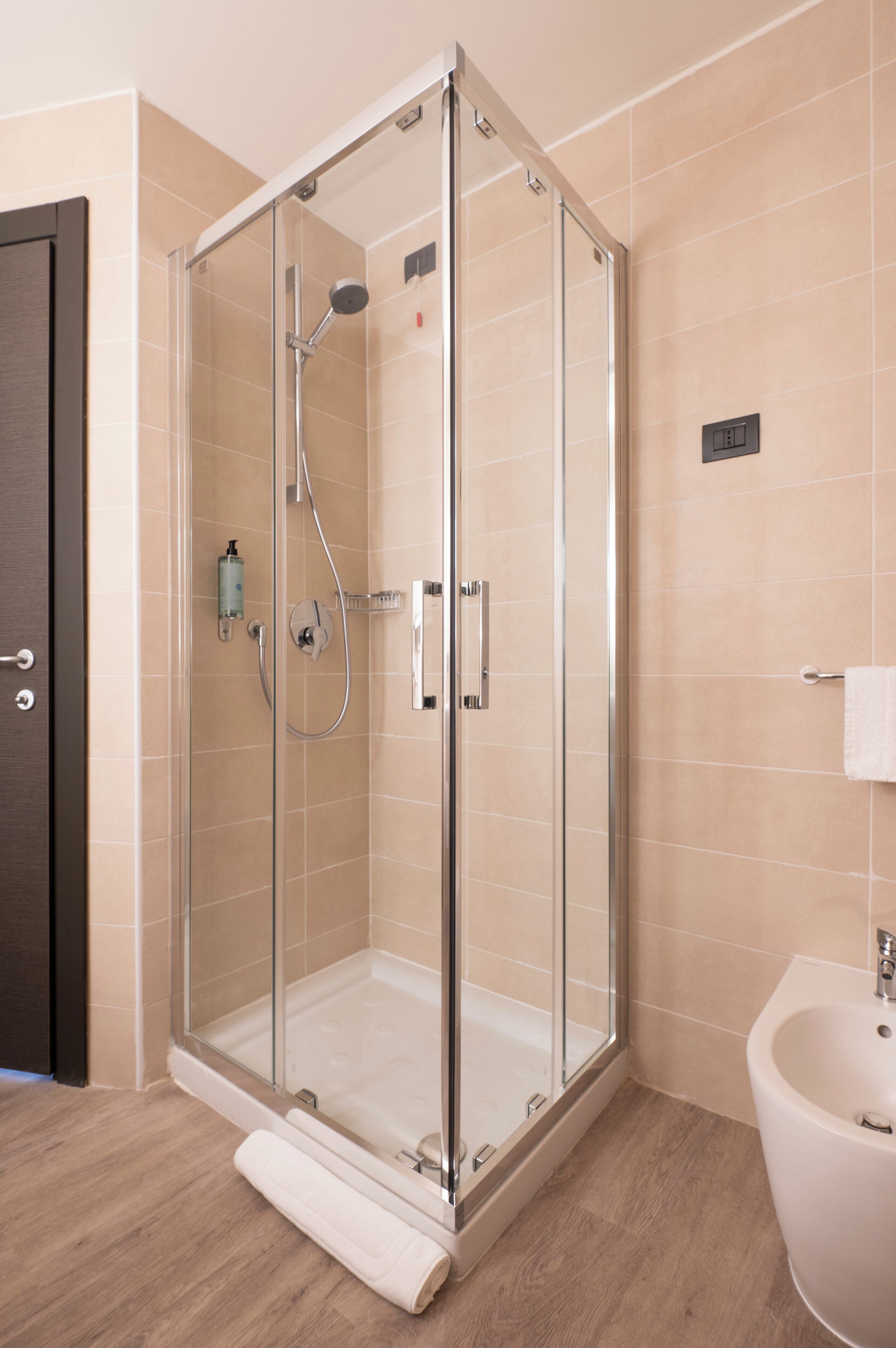 A modern bathroom with a glass-enclosed shower, a white sink, and a wooden floor.
