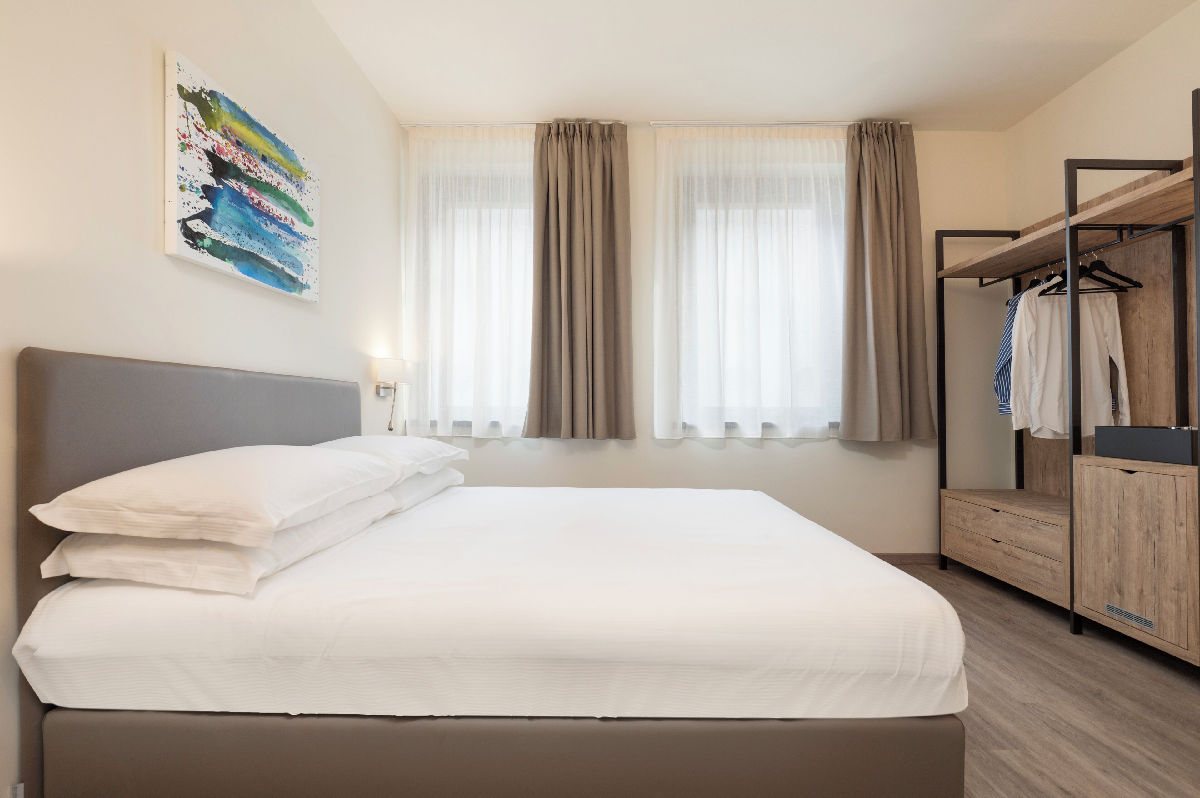Une chambre d’hôtel moderne avec un grand lit, une armoire et une fenêtre avec des rideaux.