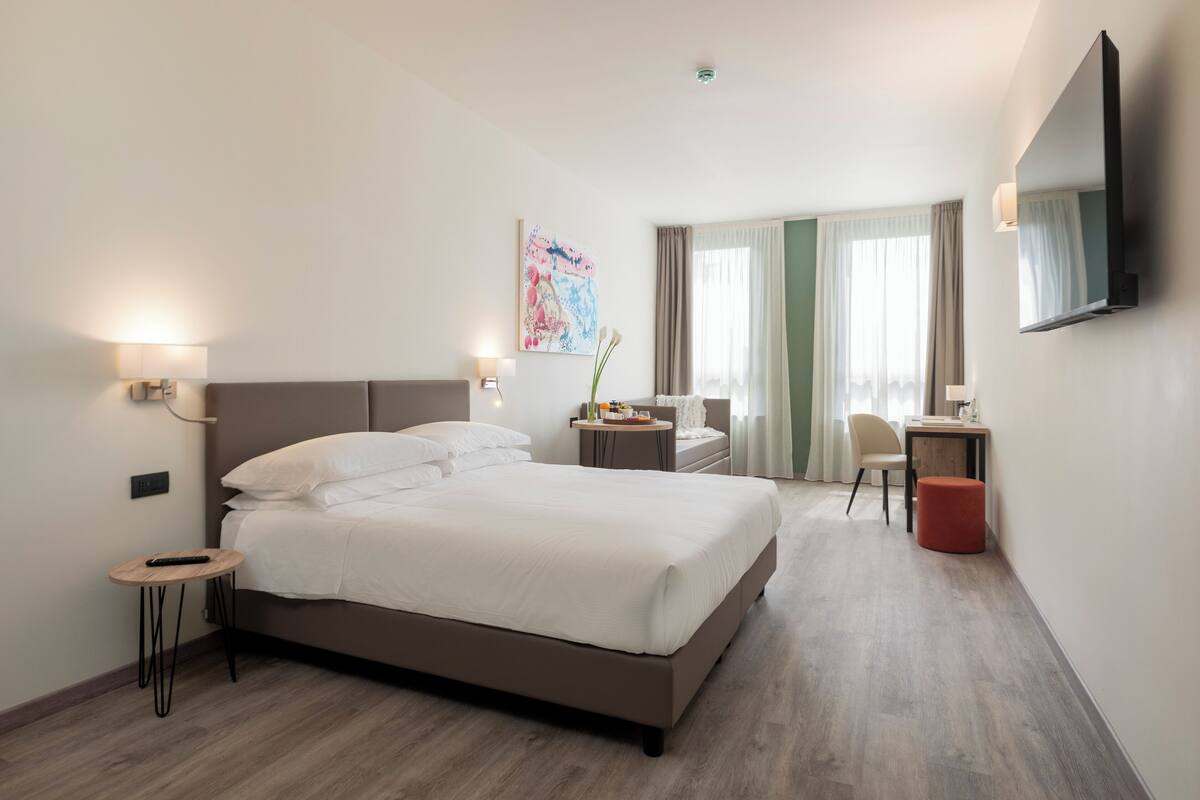 Ein modernes Hotelzimmer mit einem großen Bett, Nachttischen, einem Schreibtisch und einem Sessel.
