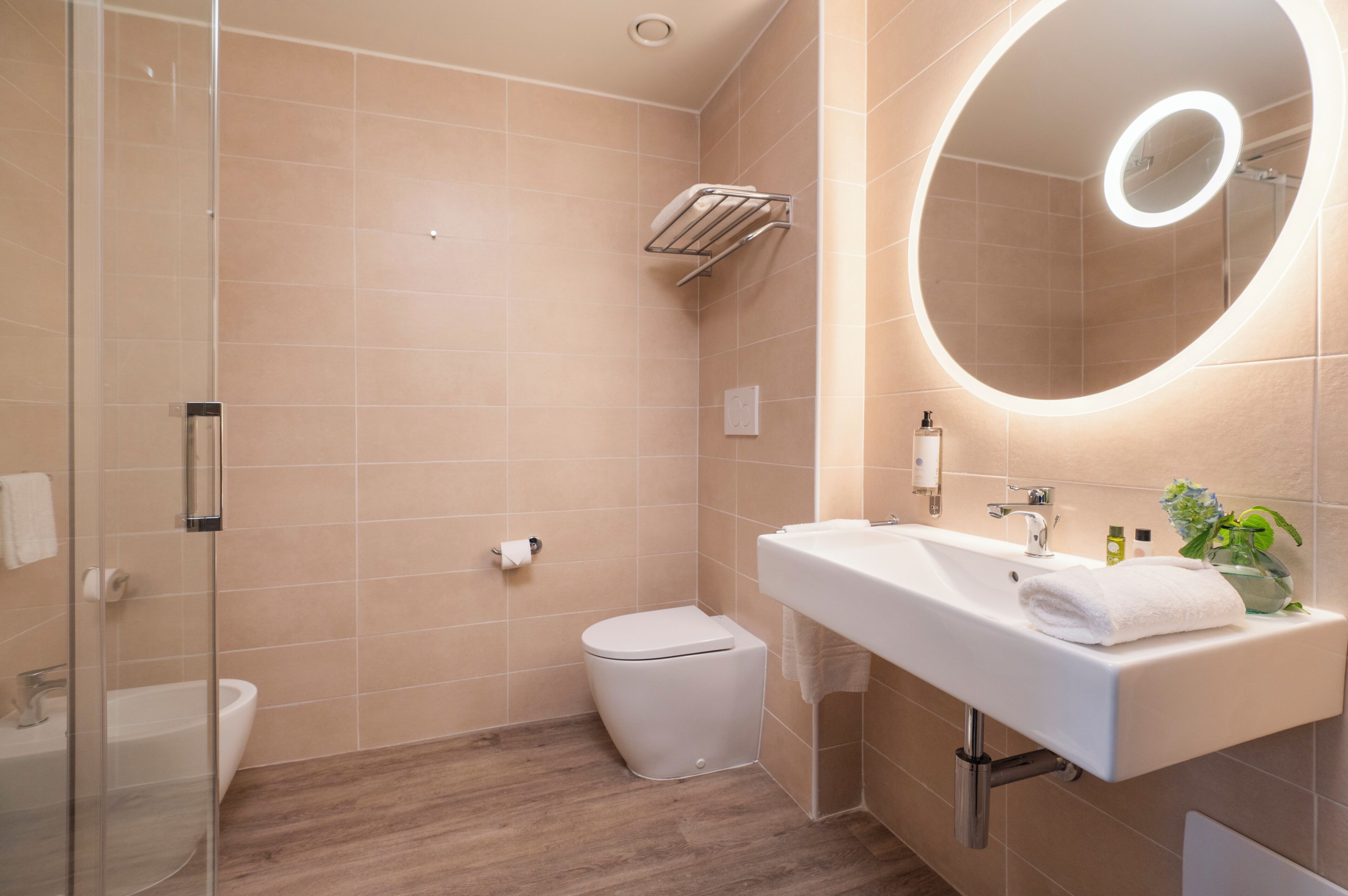 A modern bathroom with a glass shower enclosure, a white toilet, a sink with a mirror, and a towel rack.