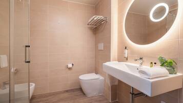 Un baño moderno con cabina de ducha de vidrio, inodoro blanco, lavabo con espejo y toallero.