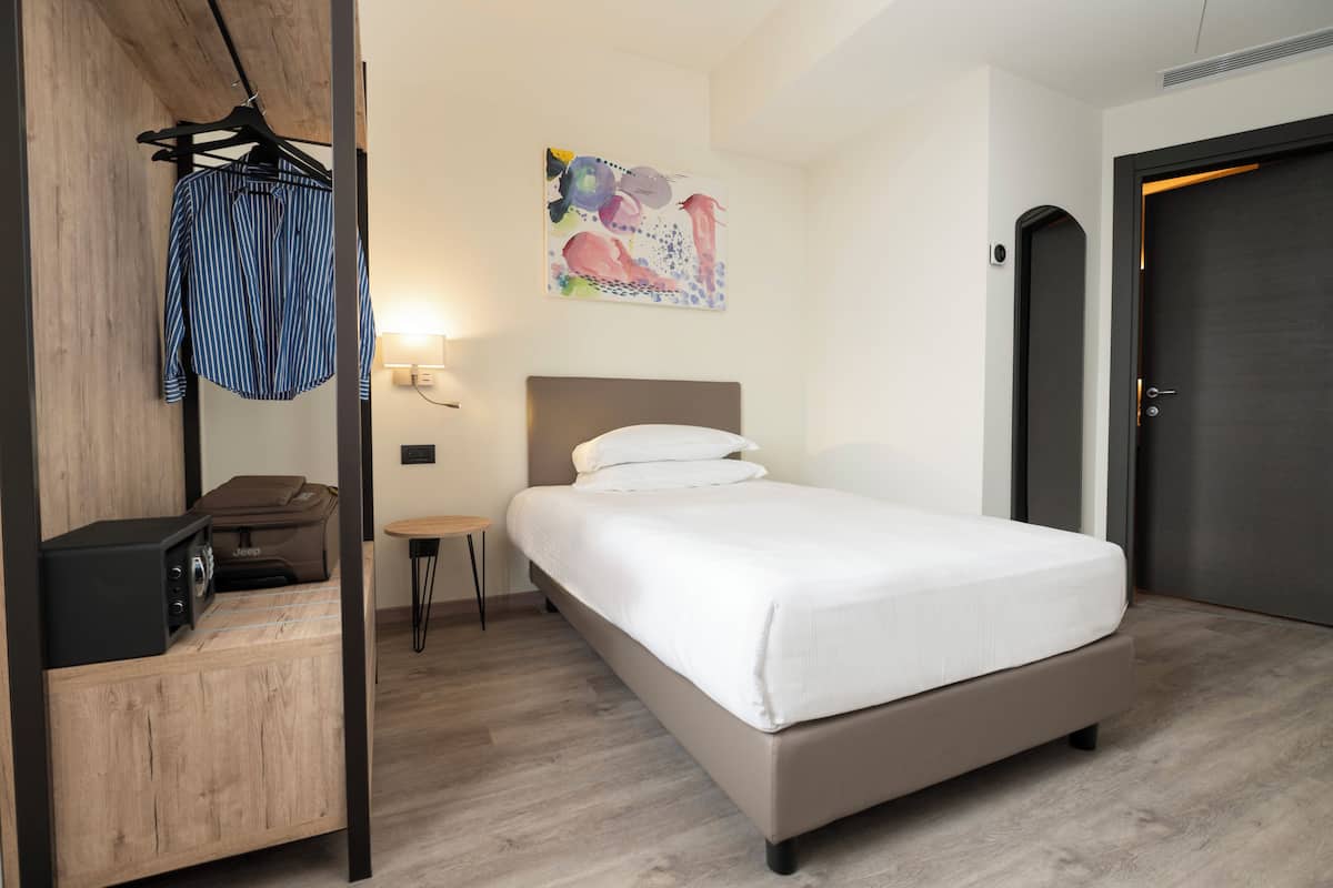 Ein Hotelzimmer mit Bett, einem Holzschrank, einem kleinen Tisch, einer Lampe und einem Bild an der Wand.
