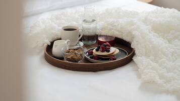 Una bandeja de desayuno ordenada sobre una cama con una colcha blanca, un almohadón blanco y un cabecero.