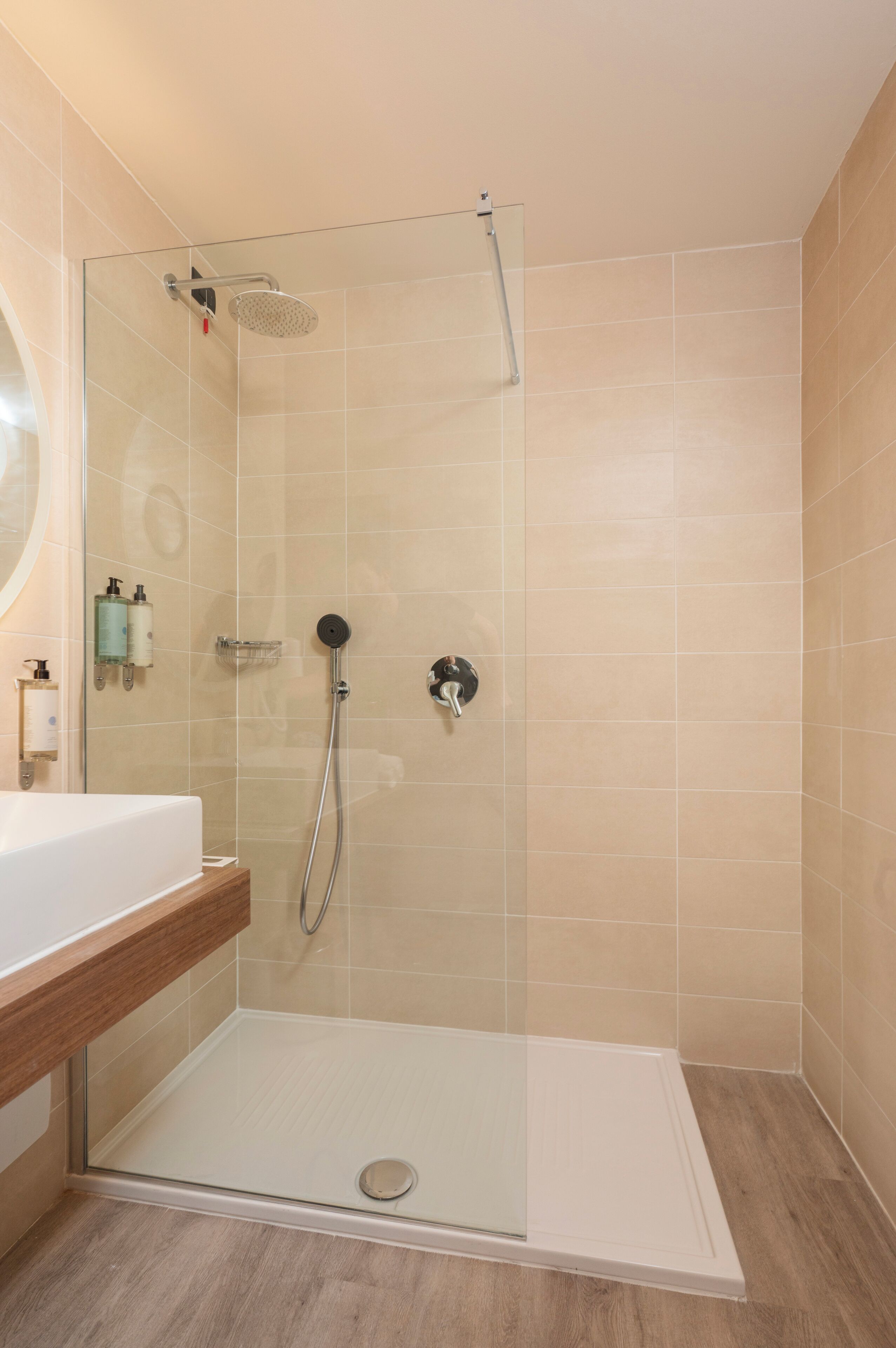 Un baño moderno con cabina de ducha de vidrio, tocador de madera y azulejos color beige.
