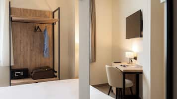 A hotel room with a bed, a desk with a chair, a coat rack with hangers, a suitcase, and a television mounted on the wall.