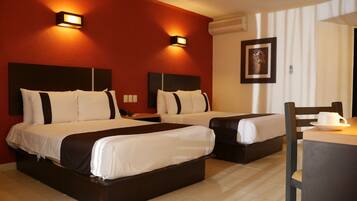 A hotel room with two beds, a desk, and a chair. There are wall-mounted lights and a framed picture on the wall.