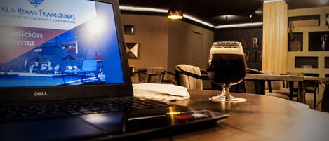 Una laptop sobre una mesa con una cerveza y un cartel al fondo.