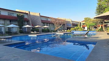 Una piscina con sillones y sombrillas, rodeada de edificios con fachadas de piedra y azulejos.
