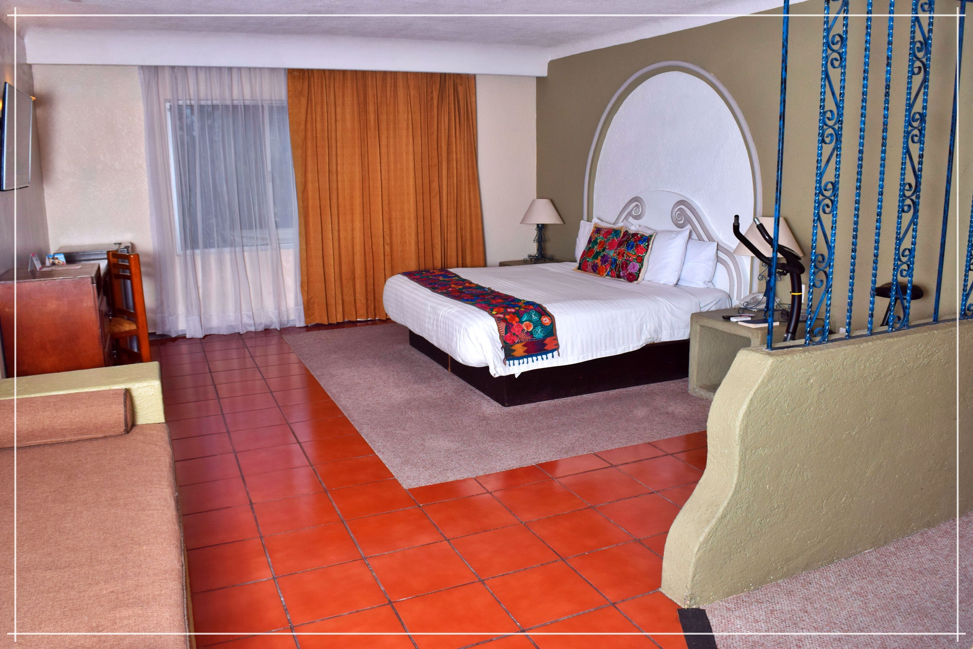 A hotel room with a bed, a desk, a chair, a window with curtains, and a decorative wall.