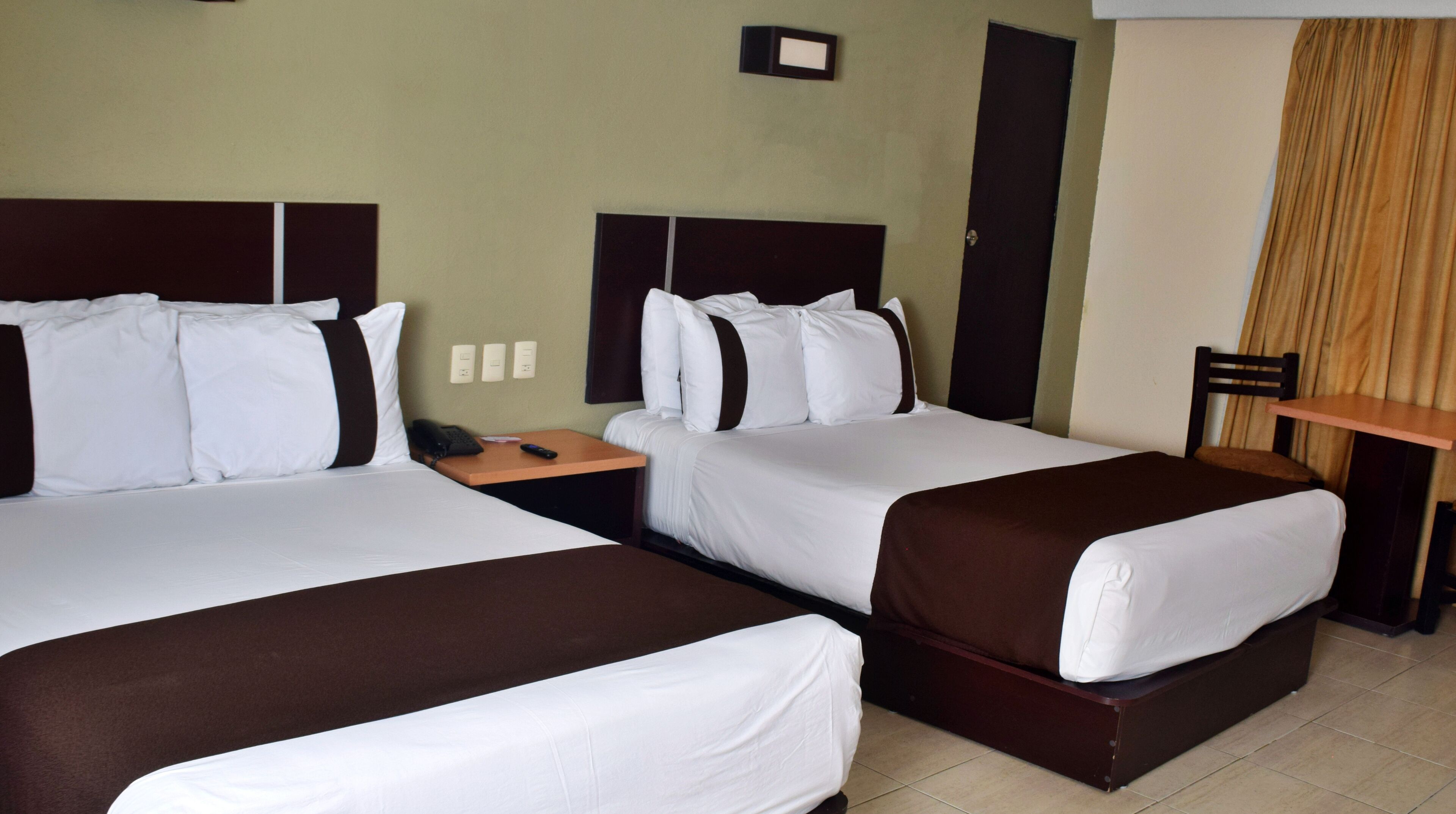 A hotel room with two beds, a nightstand, a chair, and a small table.