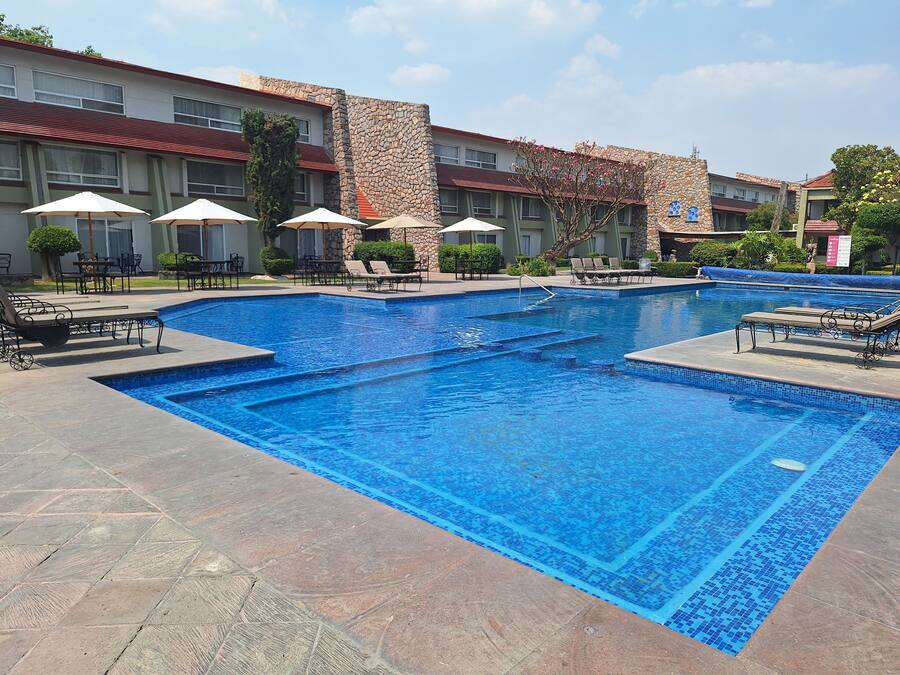 Una piscina con sillas de descanso y sombrillas, rodeada de edificios de piedra y ladrillo.