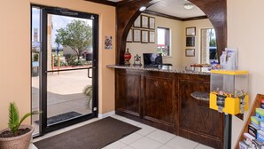A reception area with a wooden reception desk, a glass door entrance, a potted plant, and a vending machine. - Americas Best Value Inn & Suites Waller Prairie View (Waller)