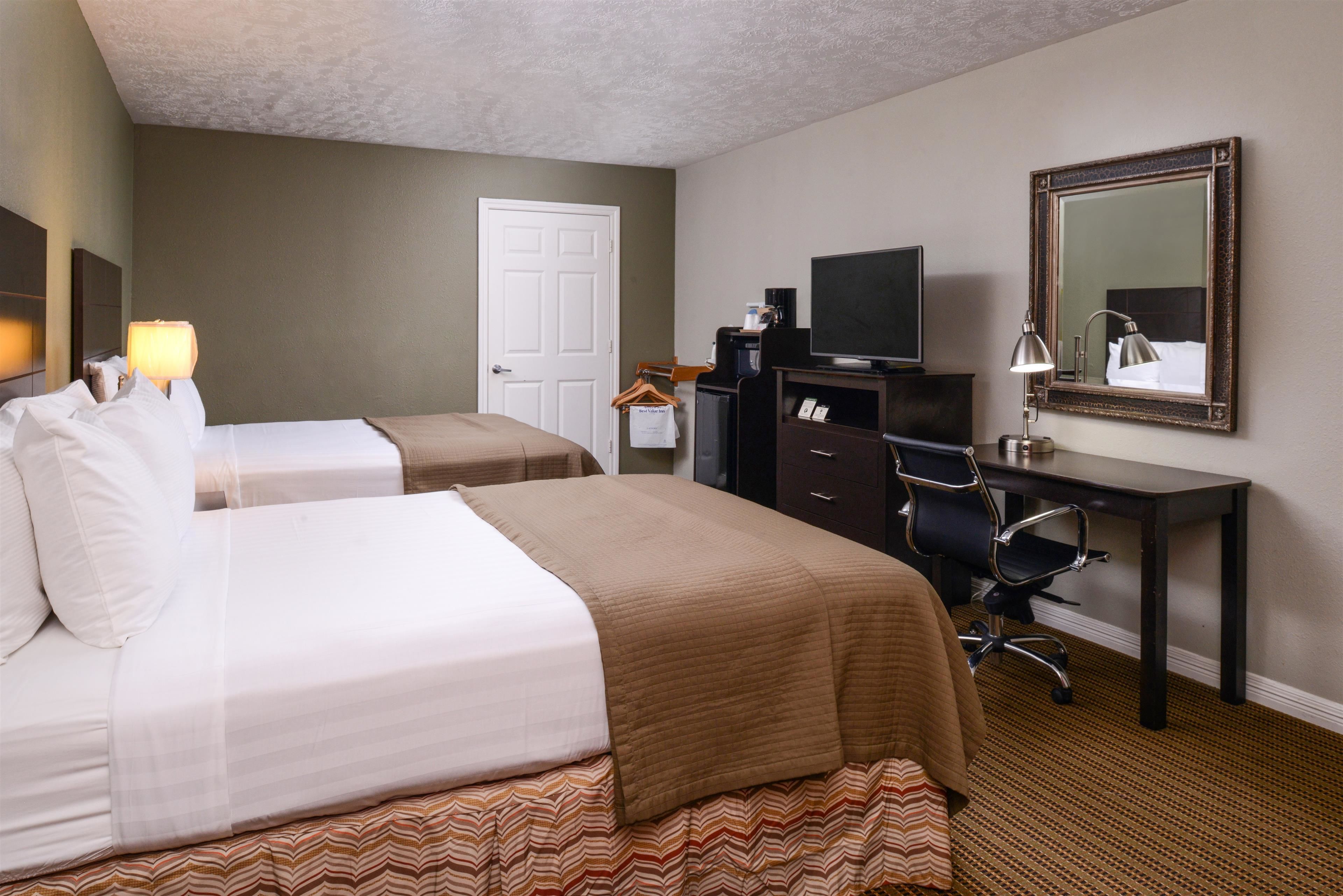 A hotel room with two beds, a desk with a computer, a TV, and a mirror.
