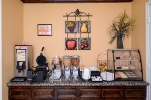 Una estación de café con una máquina de café, molinillos y una vitrina con pasteles.