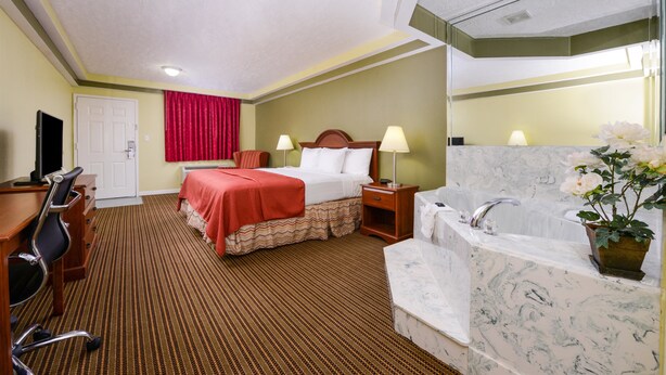 A hotel room with a bed, a desk, a chair, a bathroom with a bathtub, and a mirror. - Americas Best Value Inn & Suites Waller Prairie View (Waller)
