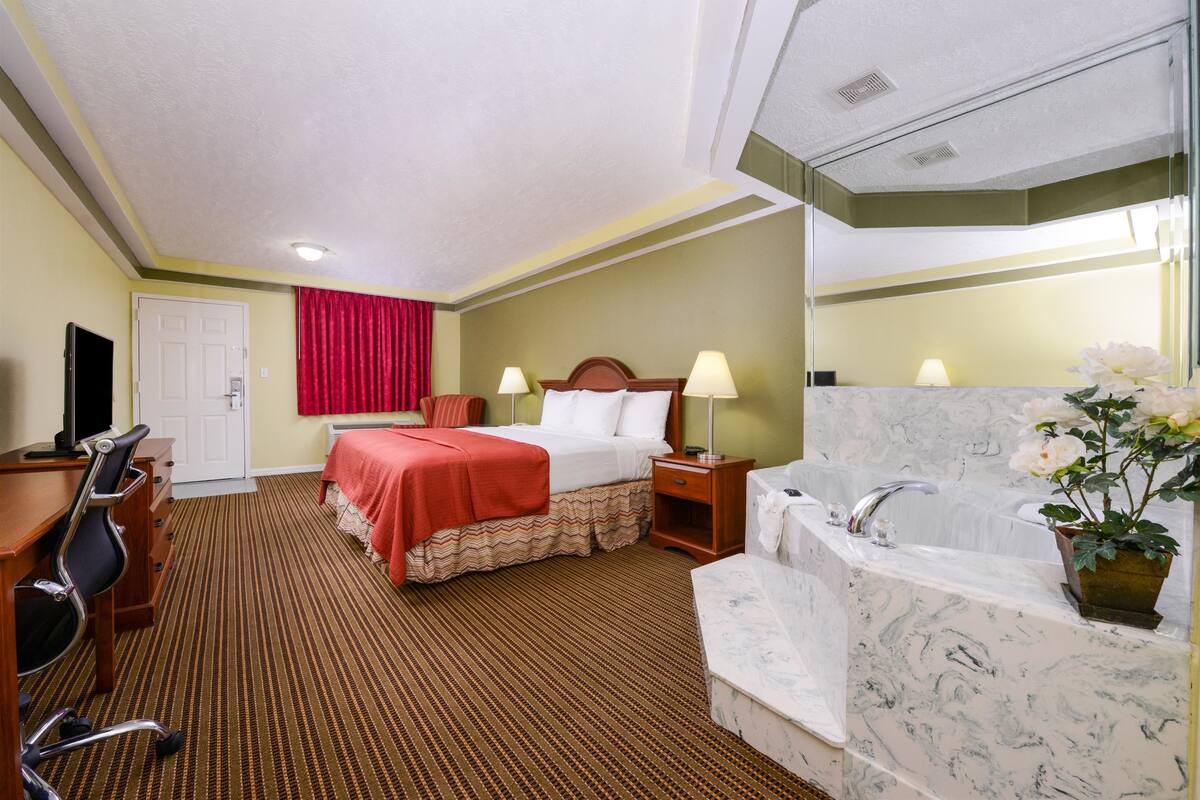 Una camera d'albergo con un letto, una scrivania, una sedia, un bagno con vasca e uno specchio.