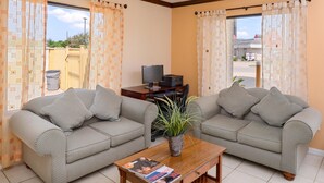 A living room with two grey patterned sofas, a wooden coffee table with a magazine, a small plant, and a TV stand with a television. - Americas Best Value Inn & Suites Waller Prairie View (Waller)