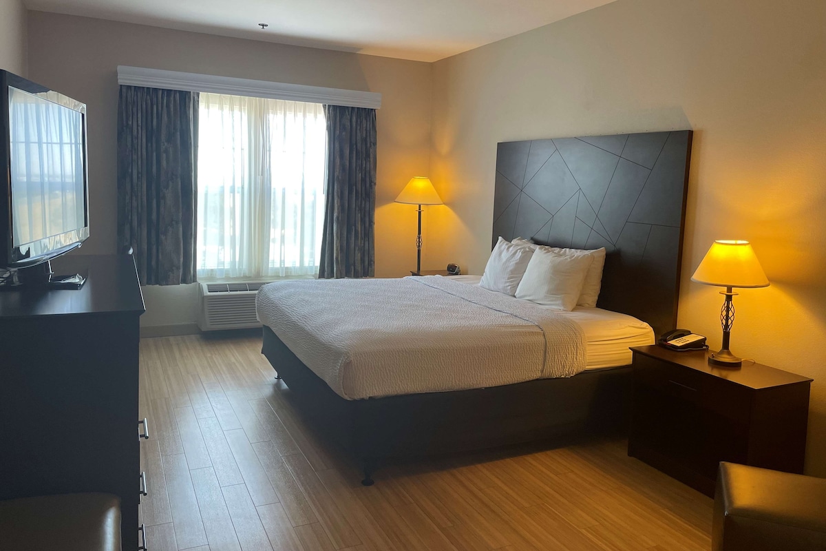 A hotel room with a large bed, two bedside lamps, a TV, and a window with curtains.