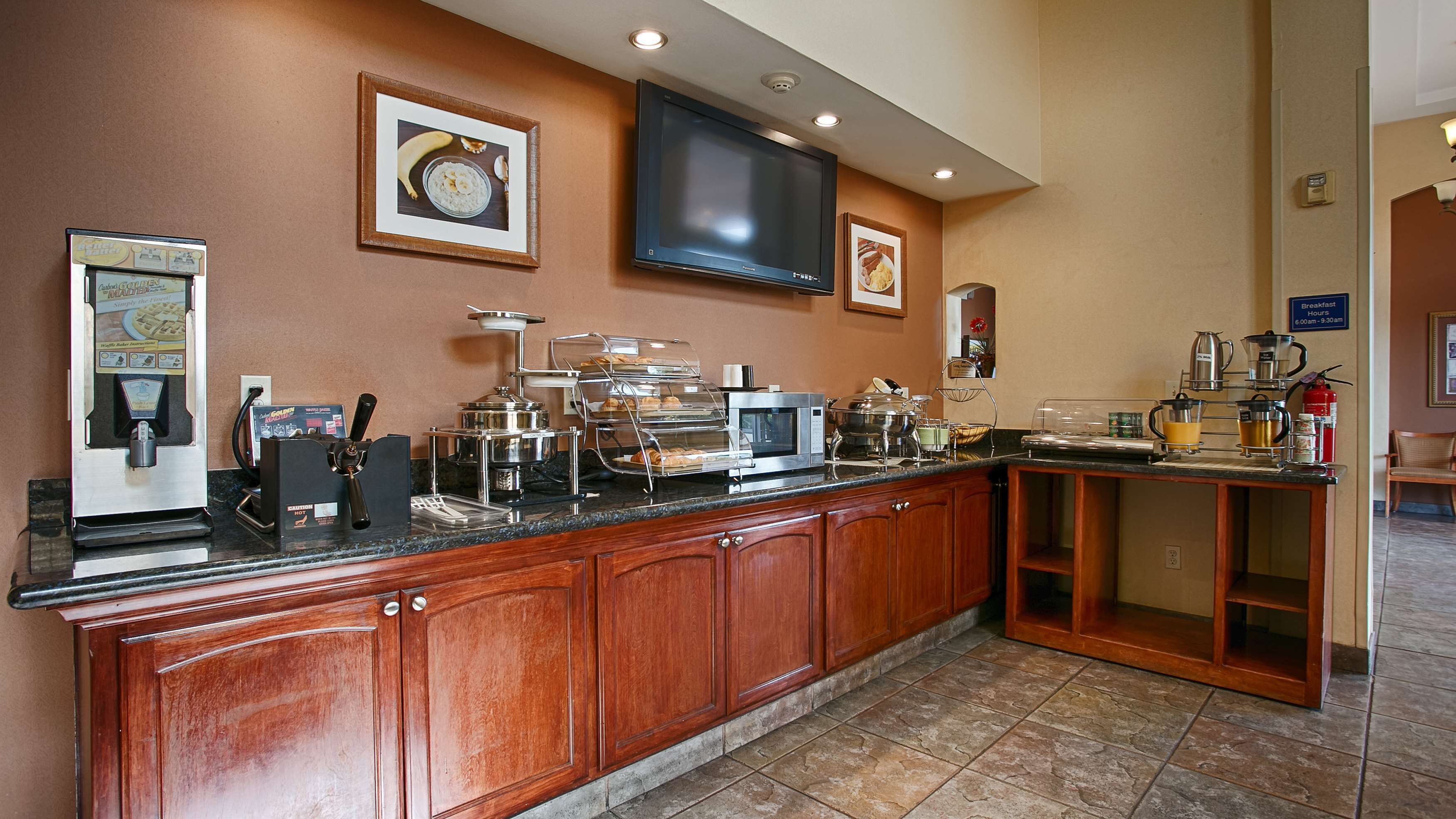 A hotel breakfast area with a self-service station, microwave, coffee maker, and a TV mounted on the wall.