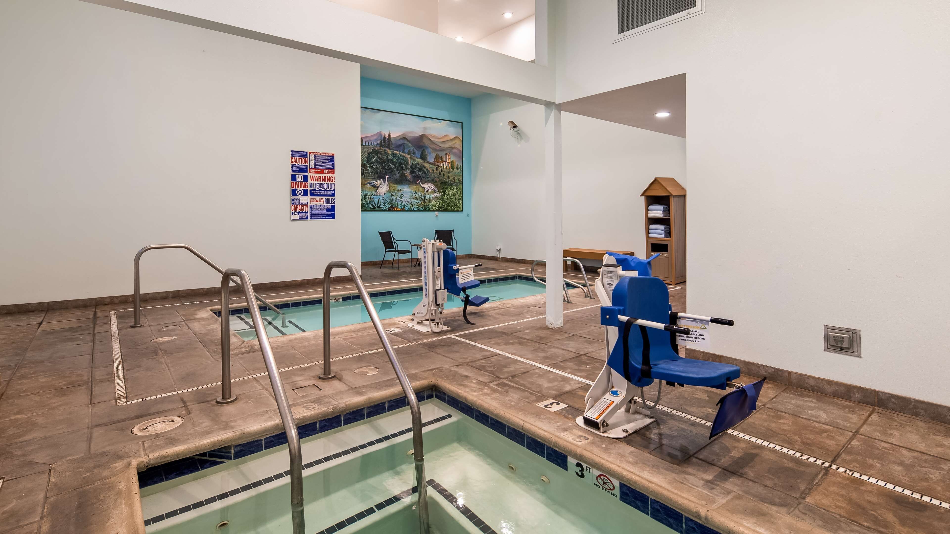 Zona de piscina con silla de salvavidas, elevador para piscina y señal de prohibido sumergirse.