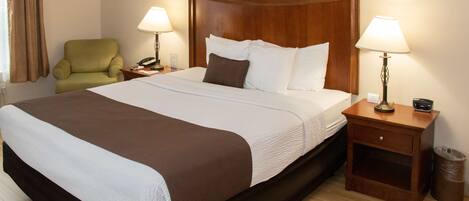 Habitación de hotel con una cama grande, dos mesitas de noche con lámparas, un sillón verde y un cabecero de madera.