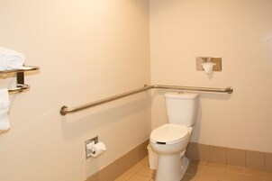 Un baño con inodoro blanco, barra de apoyo, toallero y dispensador de papel higiénico.