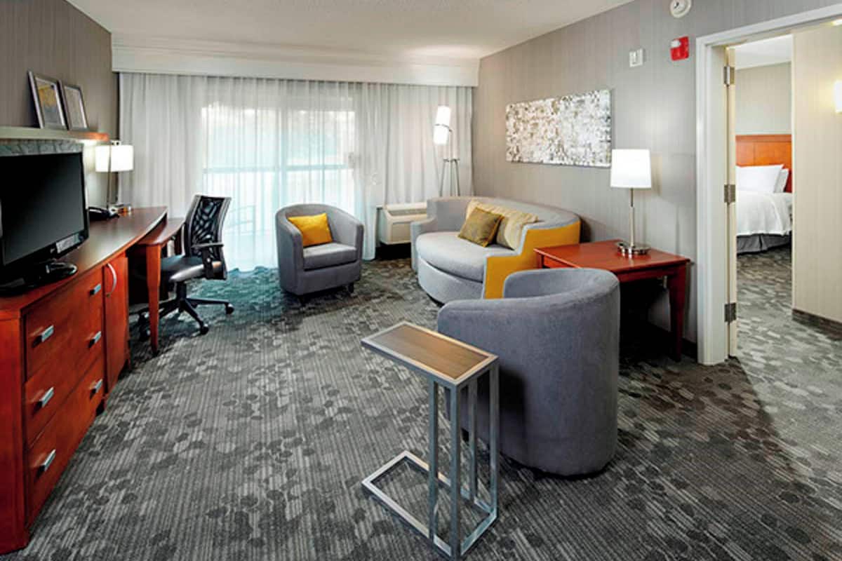 A hotel room with a TV, a desk, a sofa, a chair, and a small table.