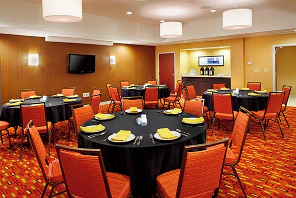 A conference room with multiple tables and chairs, a television on the wall, and a reception area in the background.