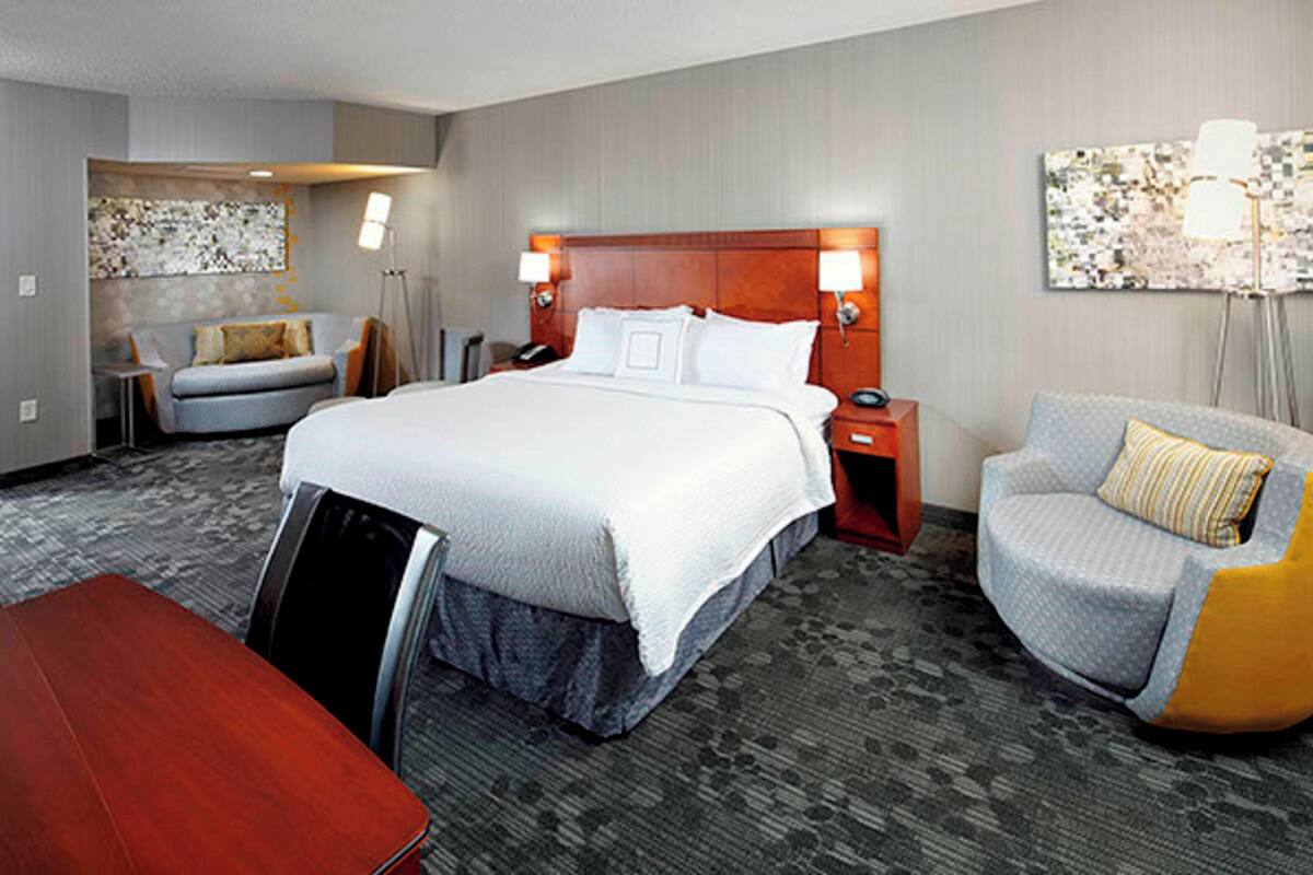 A hotel room with a large bed, a desk, a chair, and a sofa.