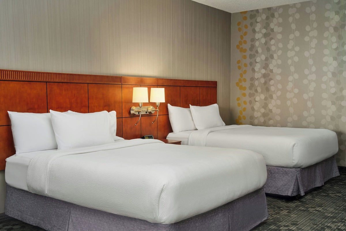 A hotel room with two beds, a wooden headboard, two bedside lamps, and a patterned wallpaper on one wall.