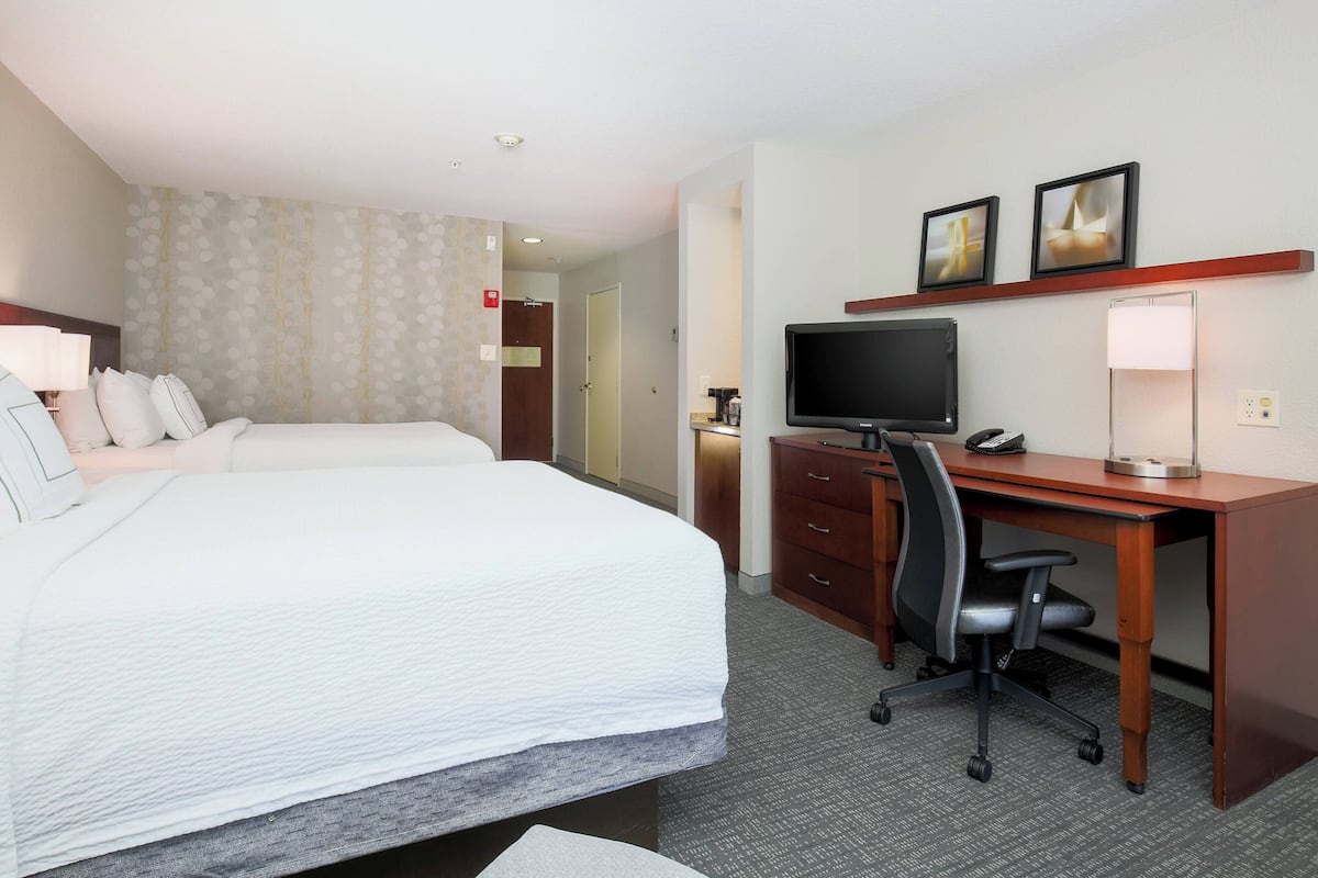 Habitación de hotel con una cama grande, un escritorio con silla, un televisor y una mesita de noche con lámpara.