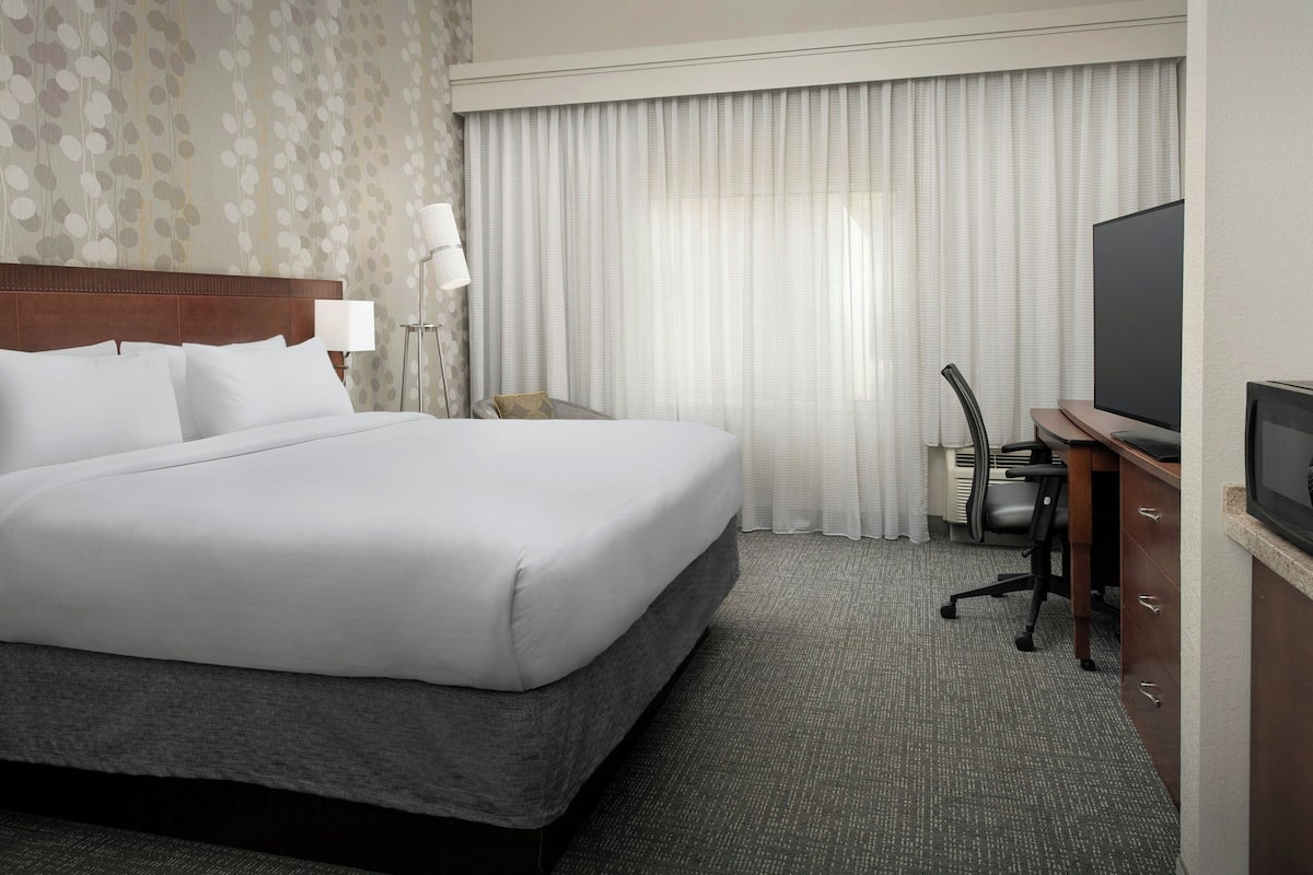 Habitación de hotel con una cama grande, un escritorio con silla, televisor y ventana con cortinas.