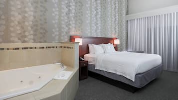 A hotel room with a large bathtub, a bed with white bedding, and a nightstand with a lamp.