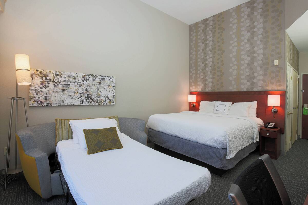 Habitación de hotel con dos camas, un escritorio, una silla, una lámpara y una pared con estampado floral.