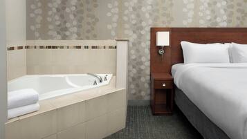 A hotel room with a bathtub, a bed, a nightstand, and a wall-mounted lamp.