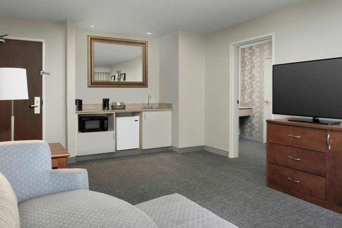 Una habitación de hotel compacta con kitchenette, televisión de pantalla plana, sofá y una pequeña mesa.