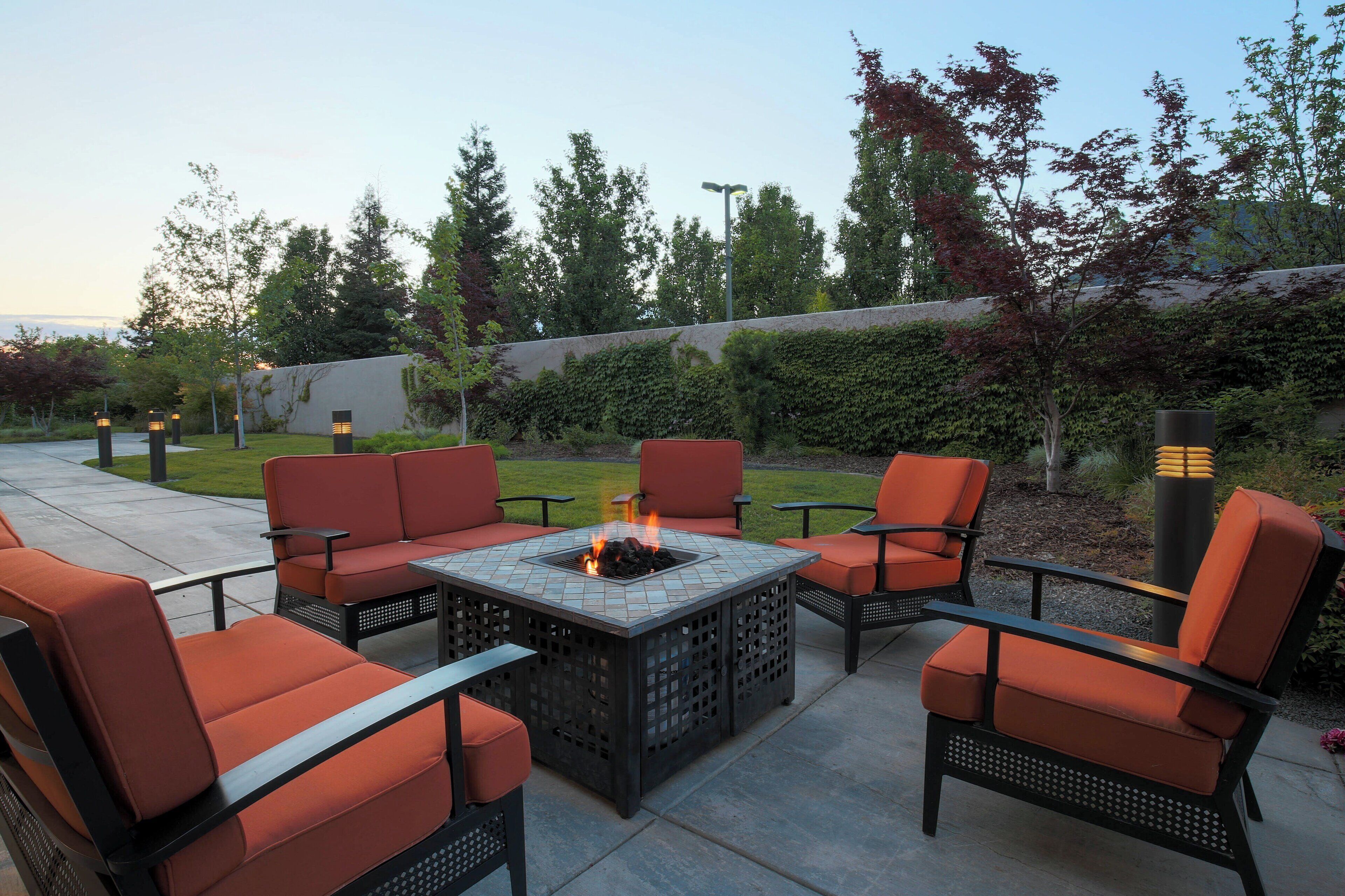 An outdoor patio area with a fire pit table surrounded by orange chairs and a tall black lamp post.