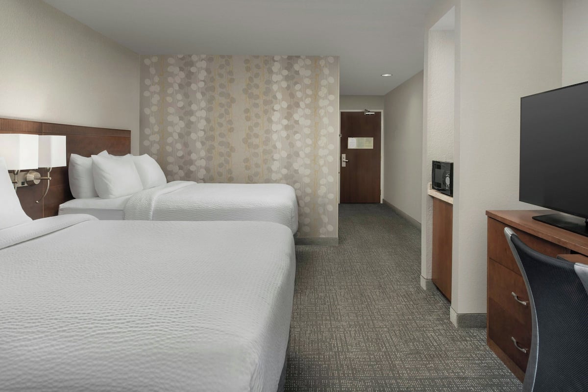 Habitación de hotel con dos camas, un escritorio con televisor y una puerta que da a un baño.