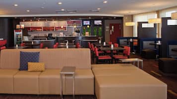 Un moderno vestíbulo de hotel con una zona de bar, áreas de descanso y una recepción.