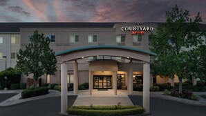 Entrada de un hotel Courtyard Marriott con un paseo techado, vegetación ajardinada y un diseño arquitectónico moderno.