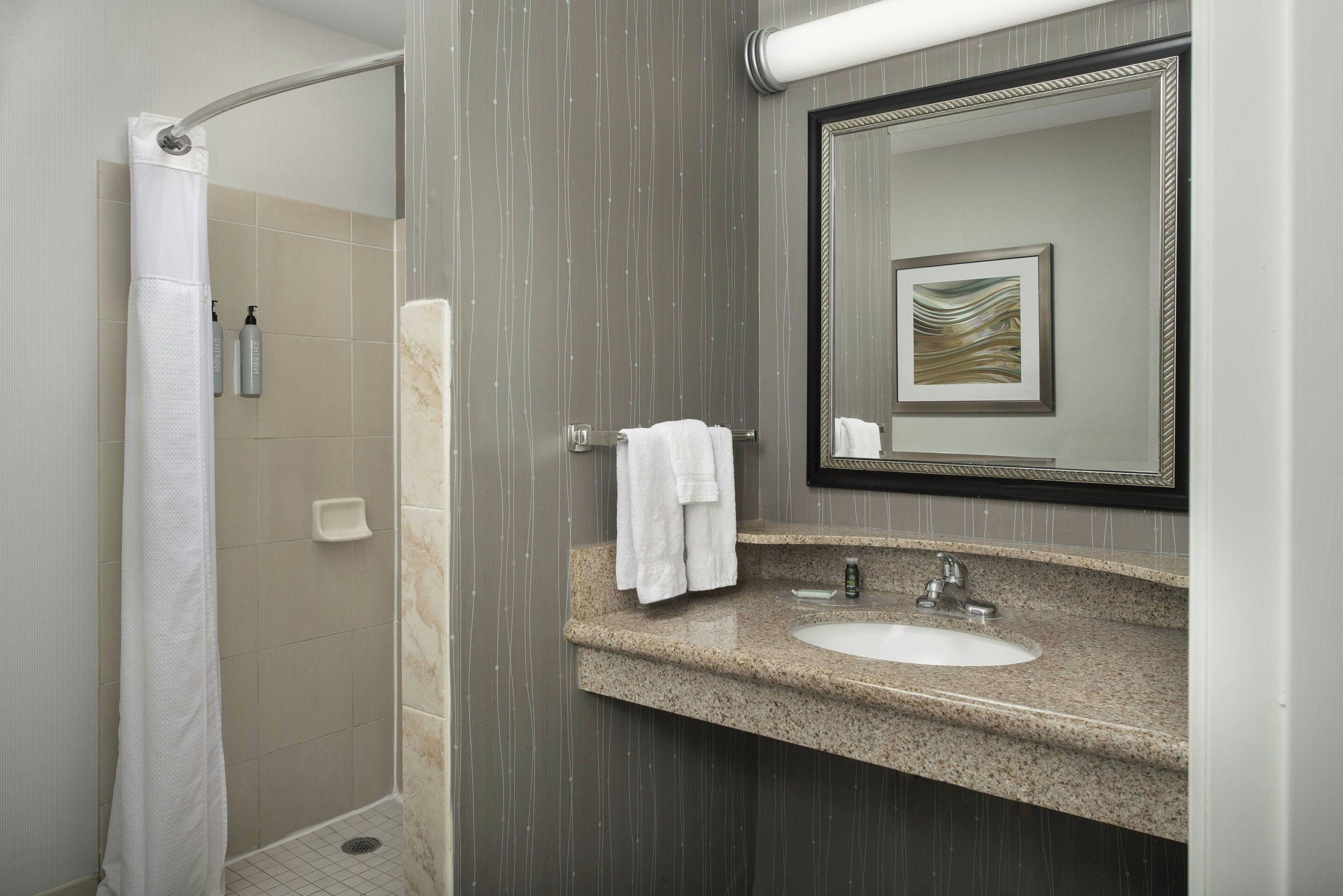 A bathroom with a shower, a sink, a mirror, and a towel rack.