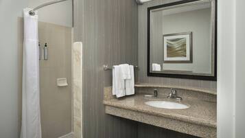 A bathroom with a shower, a sink, a mirror, and a towel rack.
