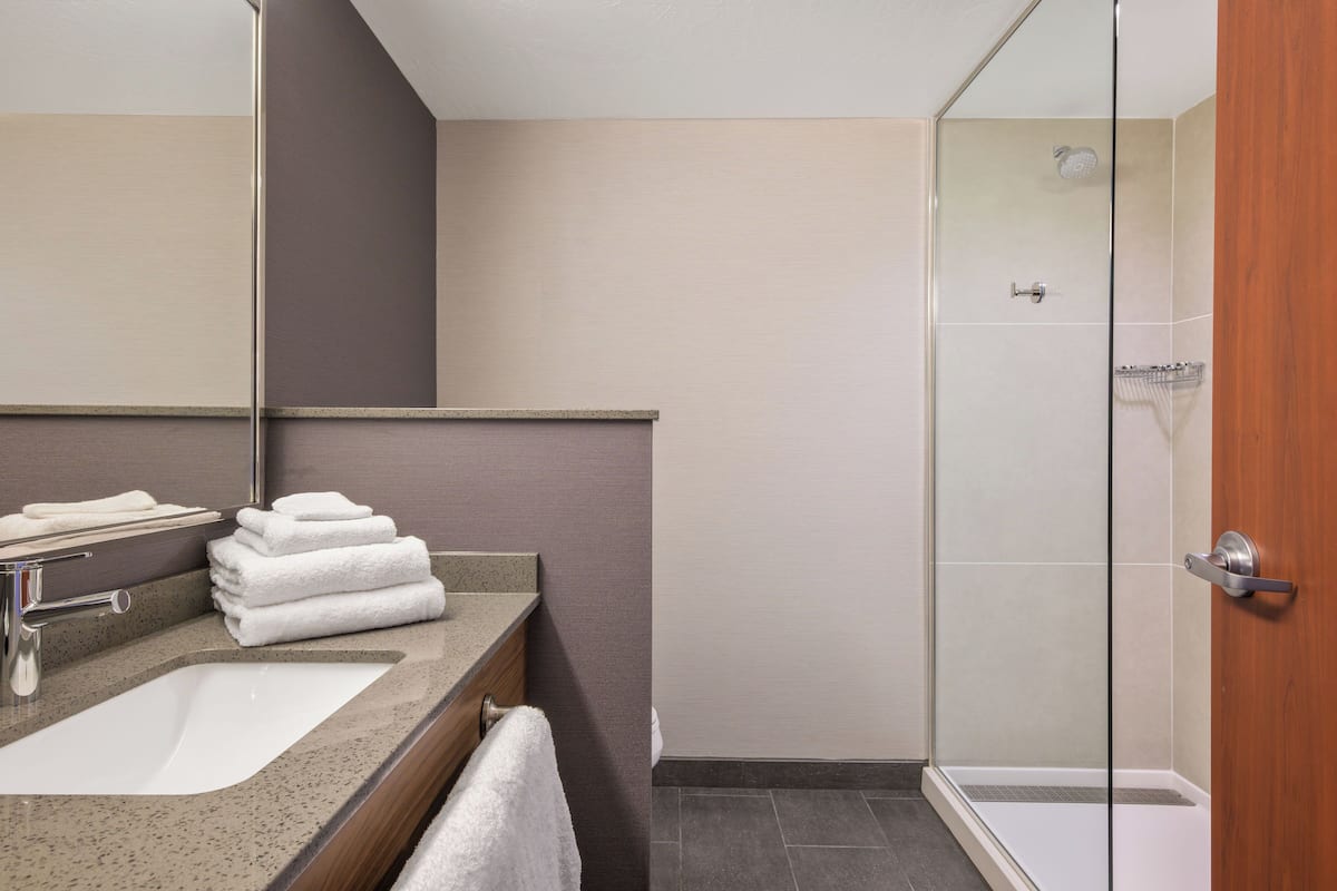 A modern bathroom with a sink, mirror, and stacked towels.