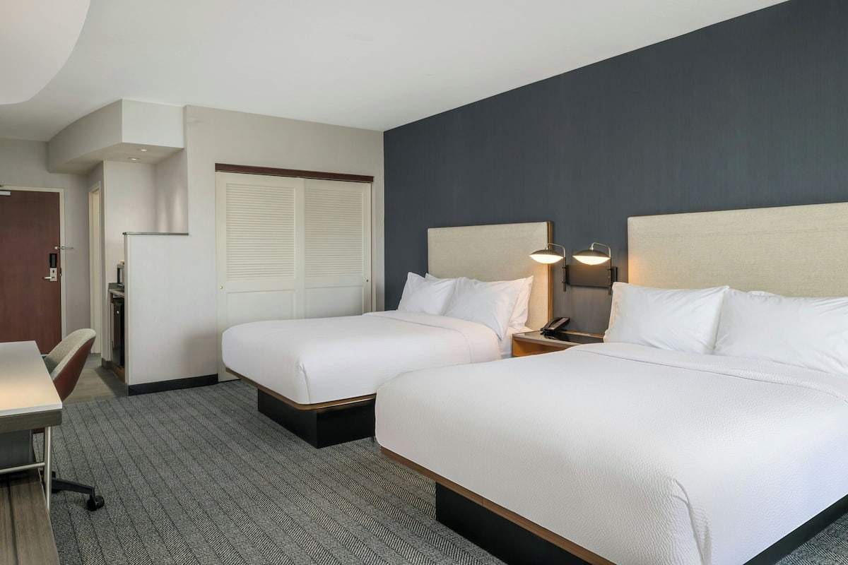 A hotel room with two beds, a desk, and a chair.
